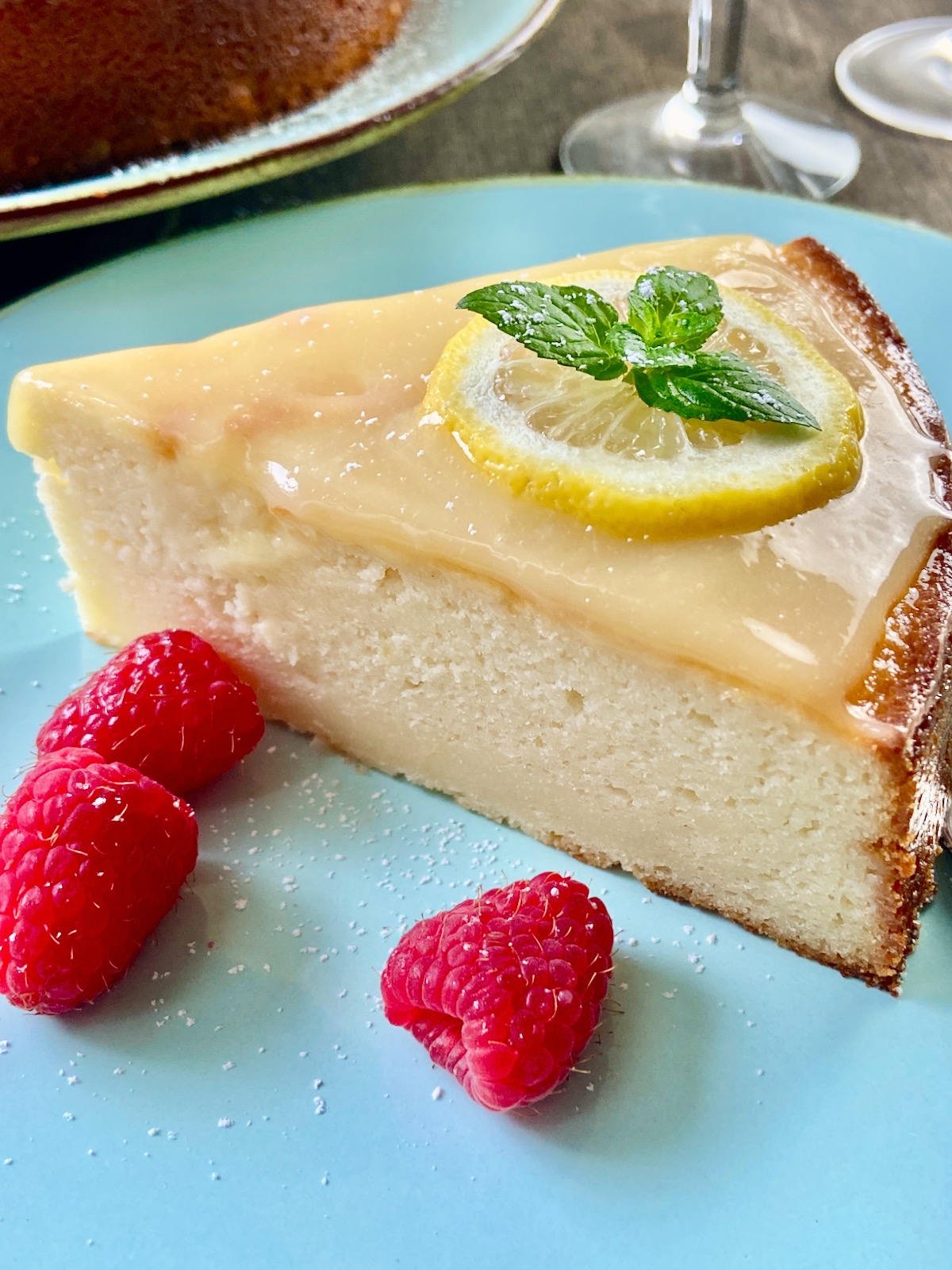 Slice of lemon Ricotta cake with lemon curd on top, garnished with a lemon slice and sprig of mint.