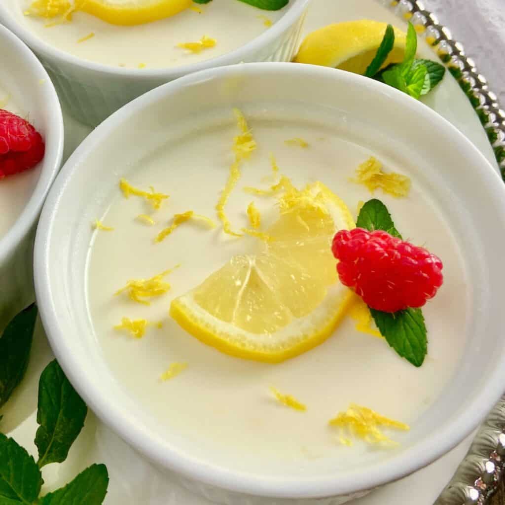 Lemon Panna Cotta in ramekin garnished with sliced lemon, a raspberry and a sprig of mint.