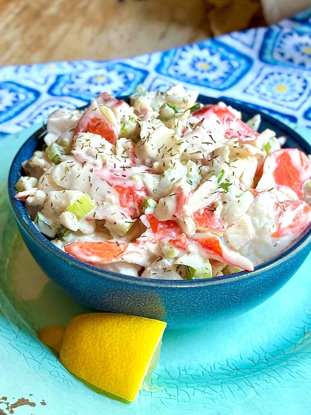 Imitation crabmeat salad in blue bowl with a slice of lemon on the side.