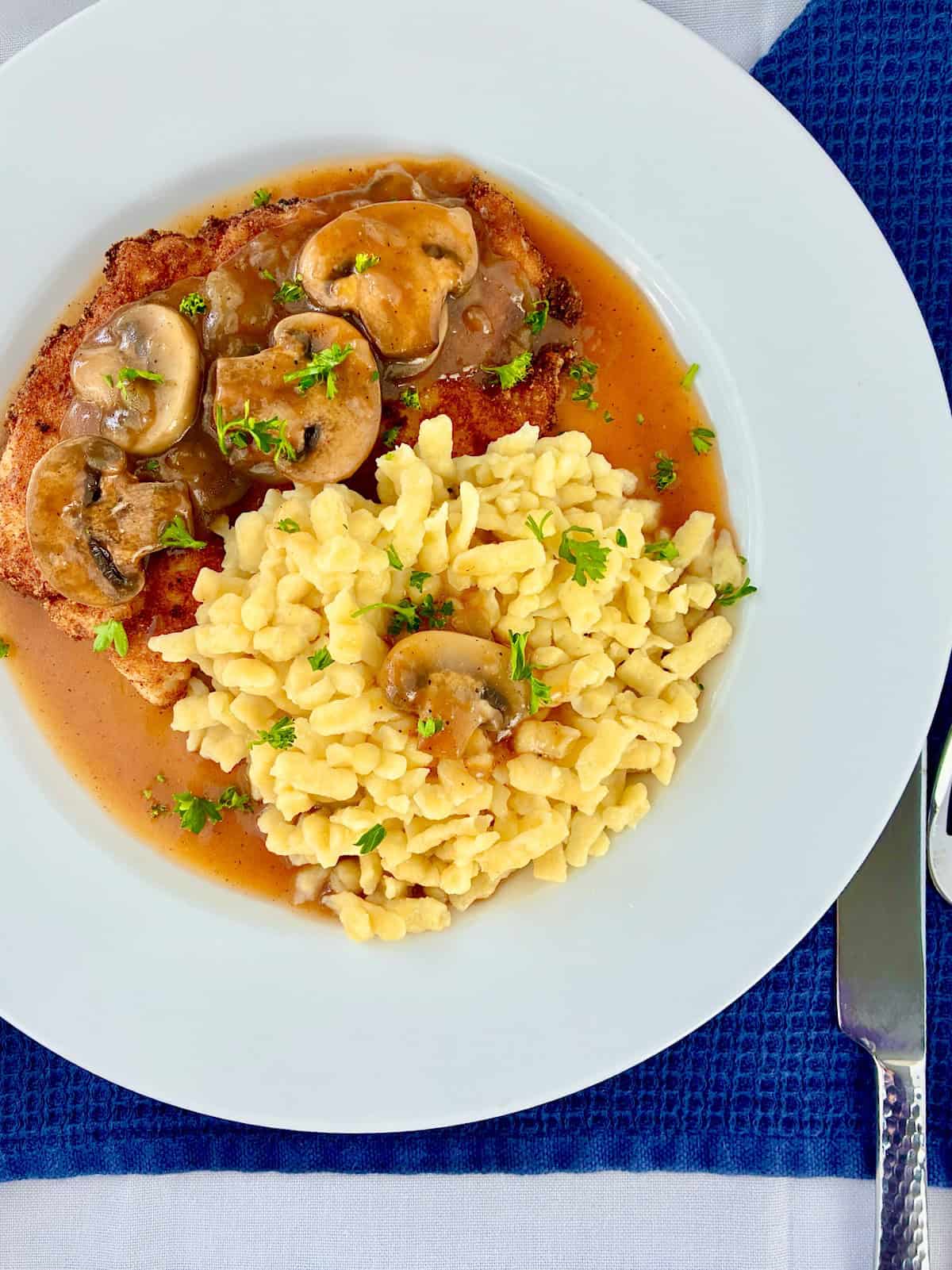 Schnitzel with mushroom gravy served with spaetzle on white plate.