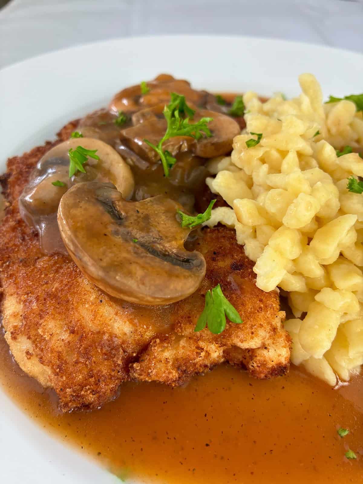 Pork Schnitzel with mushroom gravy and a side of spatzle on a white plate.