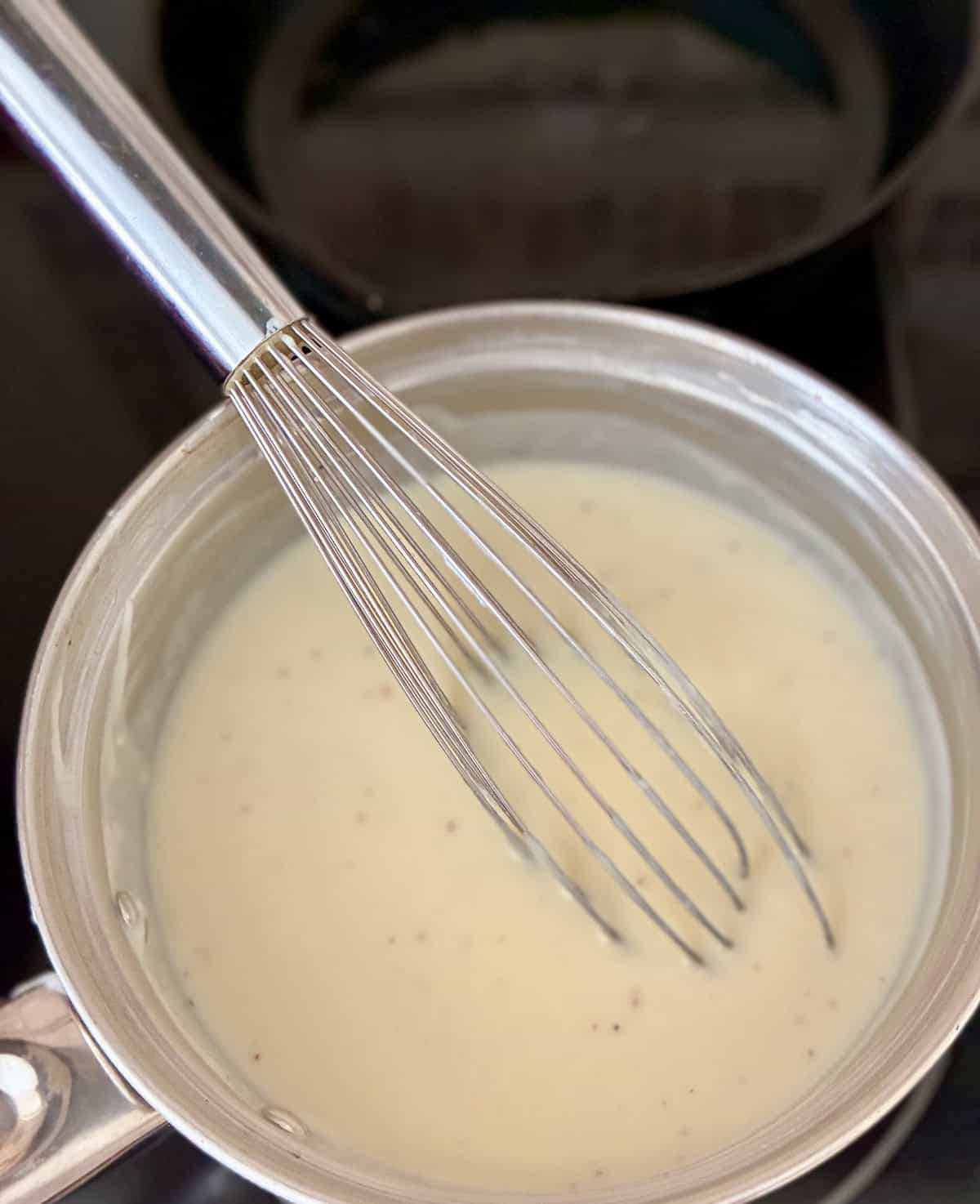 Bechamel Sauce in saucepan with wire whisk.