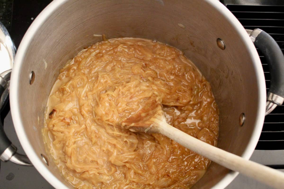 Caramelized onions in stockpot with wooden spoon.