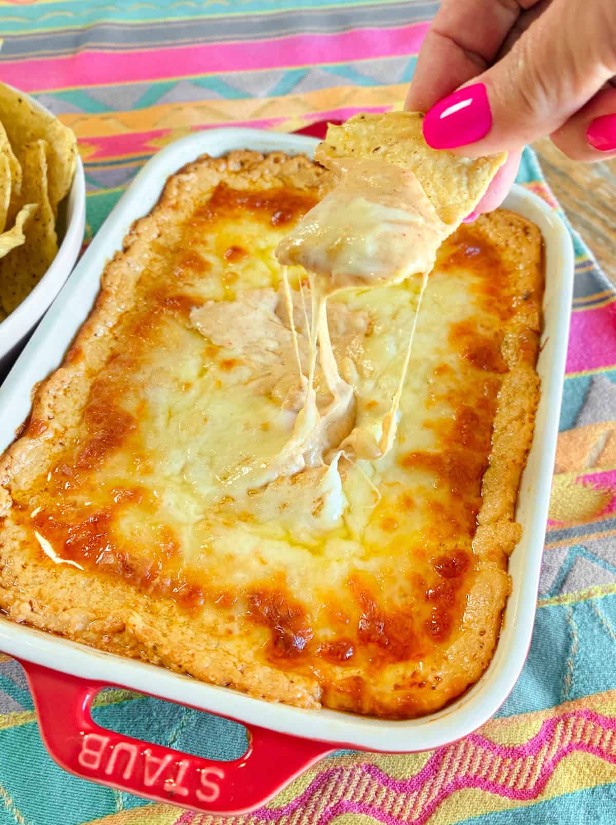 Close up of creamy cheesy enchilada dip being dipped onto a corn tortilla.