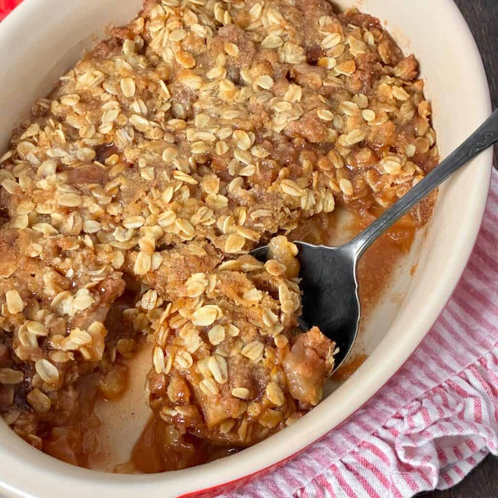 Apple crisp in oval baking dish with antique serving spoon.