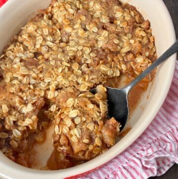 Apple crisp in oval baking dish with antique serving spoon.