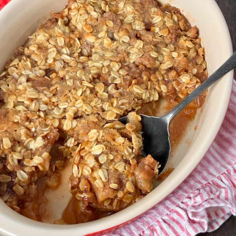 Apple crisp in oval baking dish with antique serving spoon.