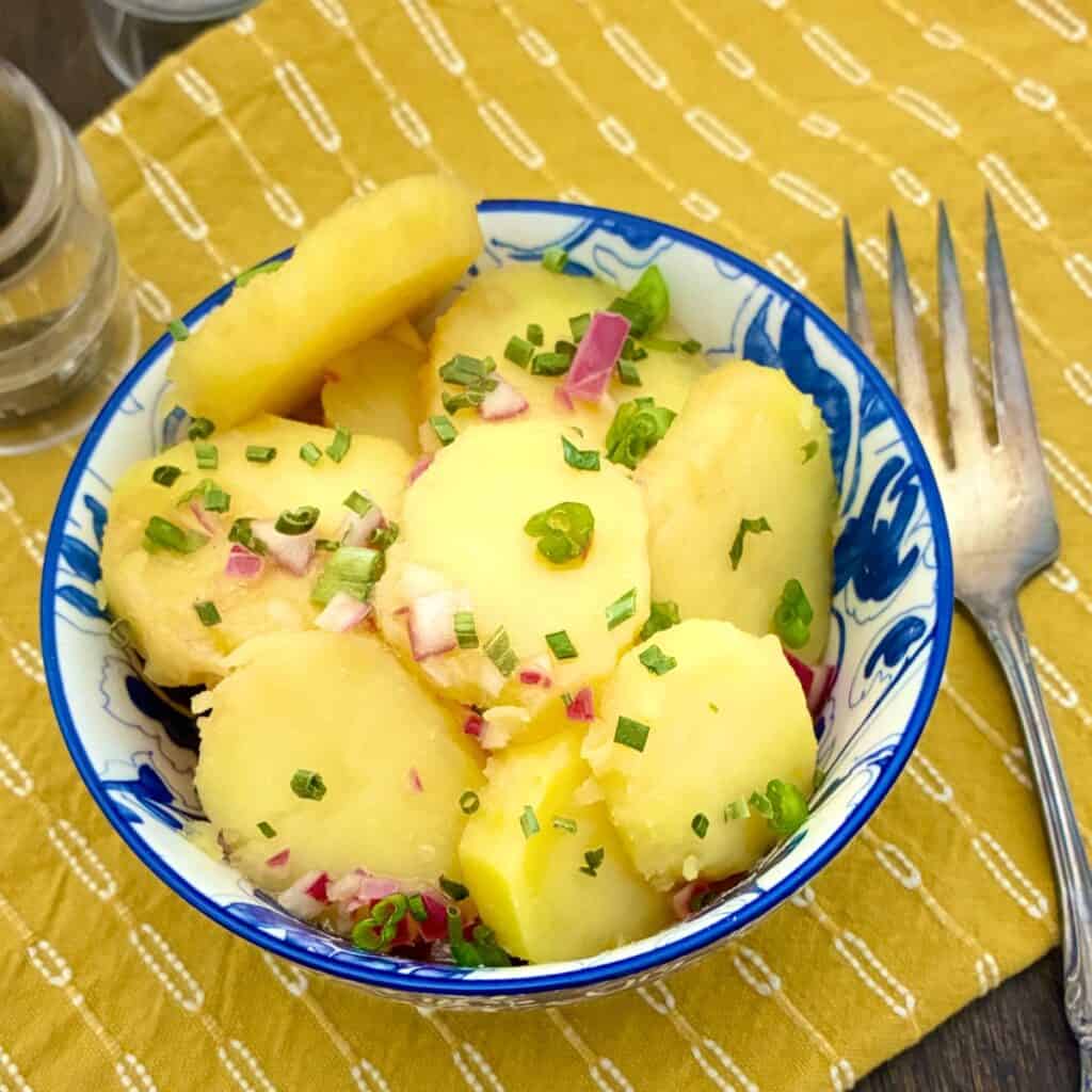 Austrian Potato Salad in decorative blue bowl, ganished with chives and red onion.