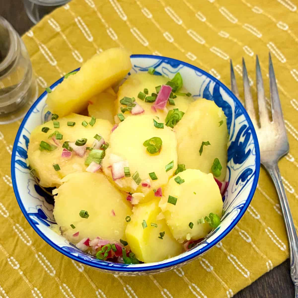 Austrian Potato Salad in decorative blue bowl, ganished with chives and red onion.