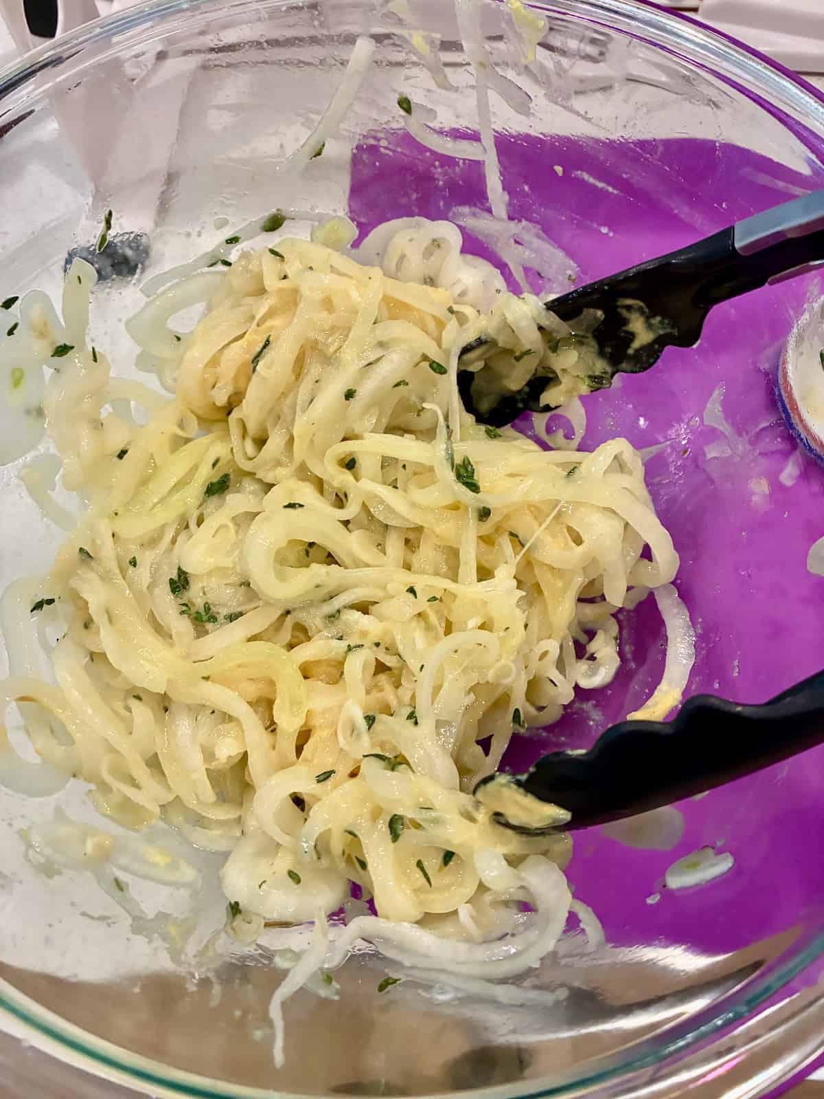 Sliced onions lightly coated with Dijon mustard in mixing bowl.