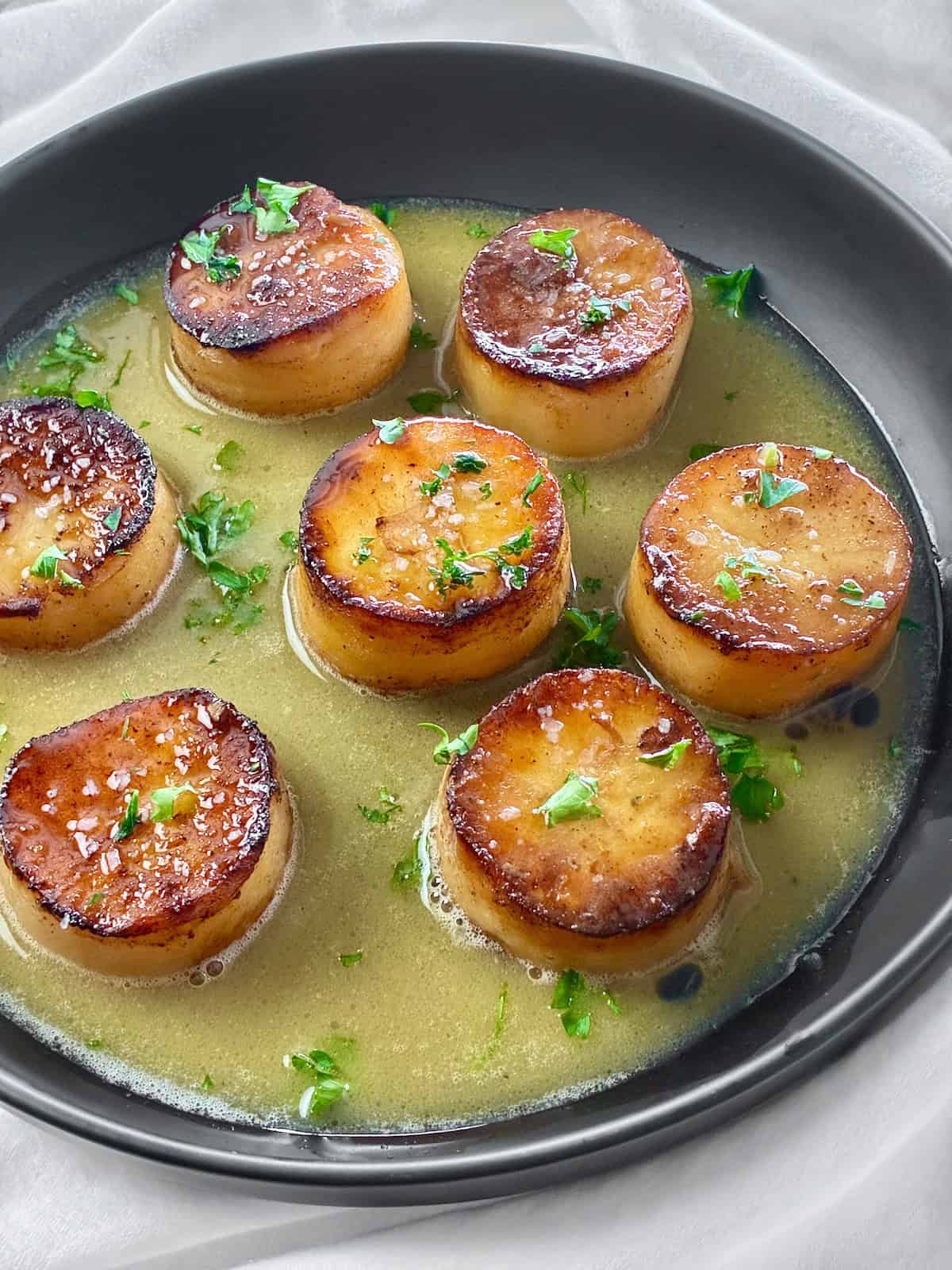 Fondant Potatoes cut in a cylinder shape in a black bowl braised with a buttery, savory broth.