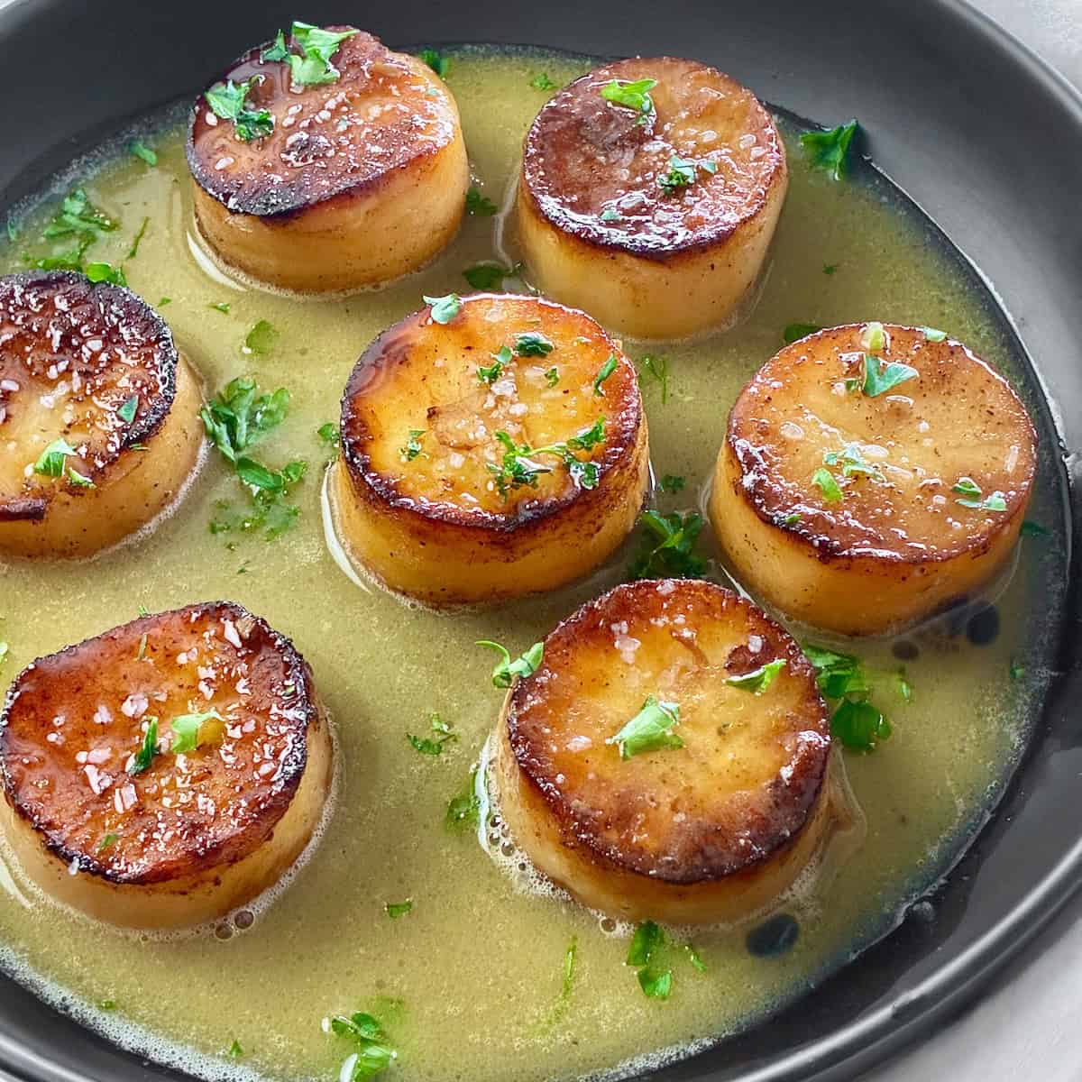 Fondant Potatoes cut in a cylinder shape in a black bowl braised with a buttery, savory broth.