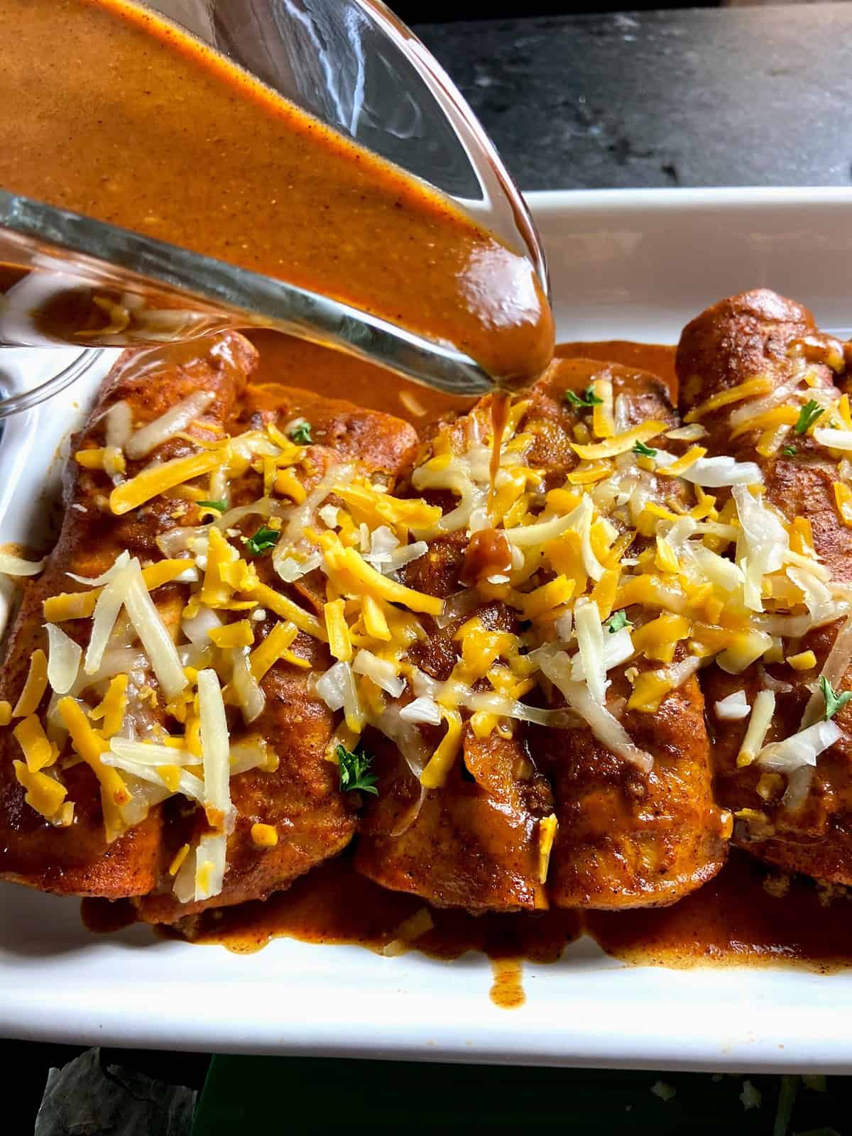 Red enchilada sauce being drizzled over enchiladas.