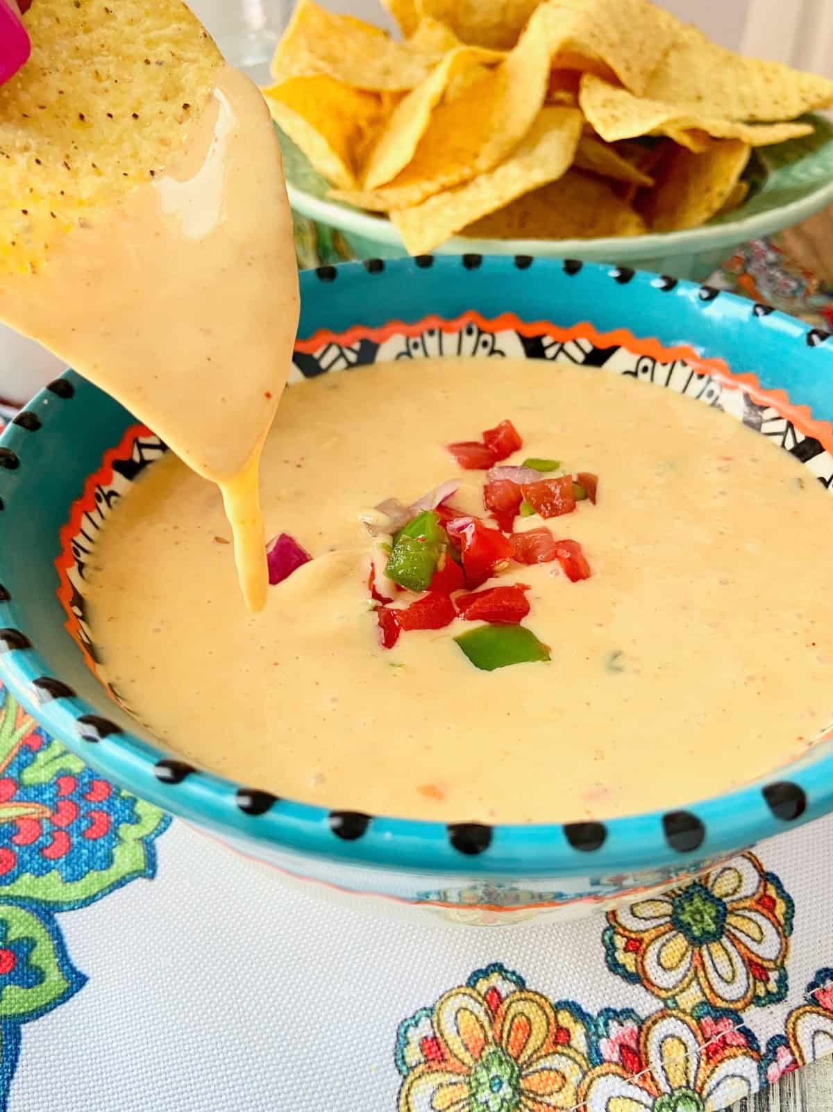 Corn tortilla chip being dipped in queso.
