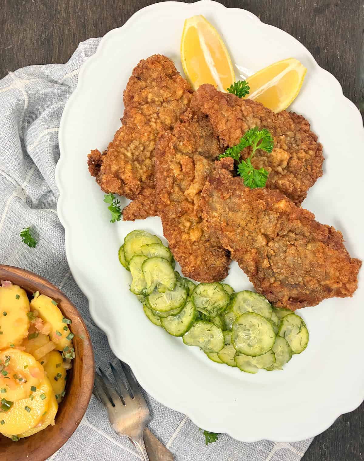 Authentic Austrian Wiener Schnitzel and dill cucumbers on white serving platter.